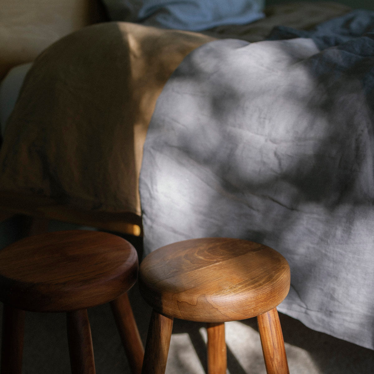 Two wooden milking stools in front of a gray textured blanket on a couch.