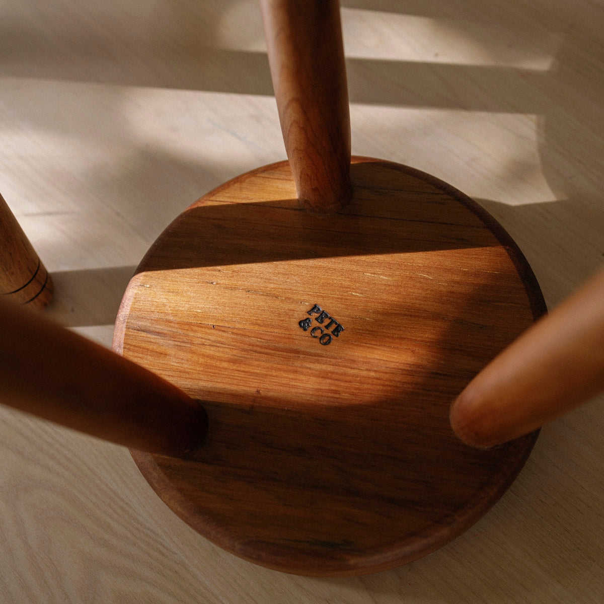 Wooden milking stool with a visible brand logo on a light wooden floor.