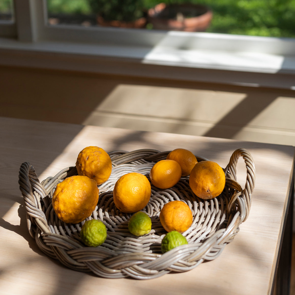 Wicker tray basket with lemons and limes on a wooden surface near a window