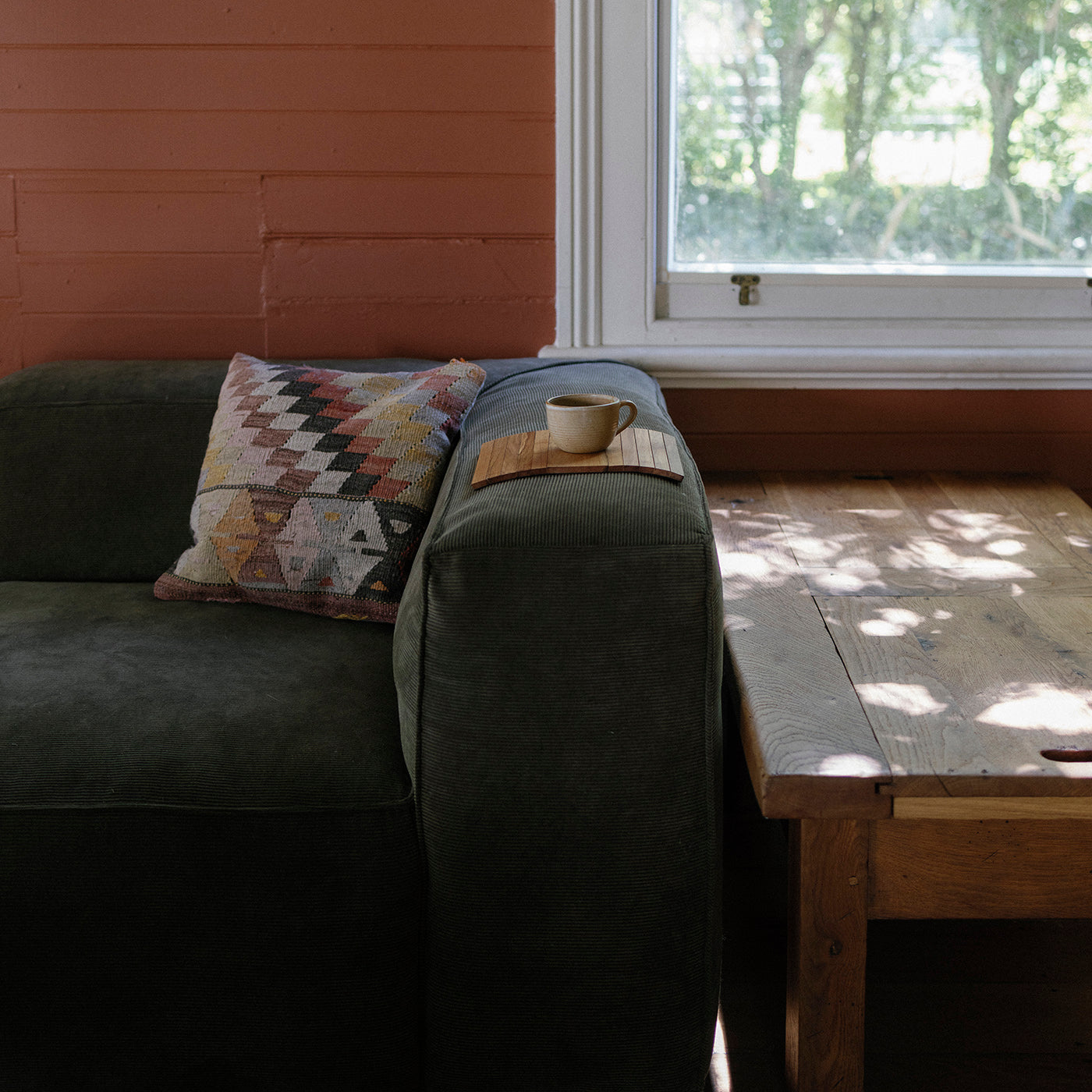 Sofa with a patterned pillow and a cup on a wooden sofa table in a room with a window.