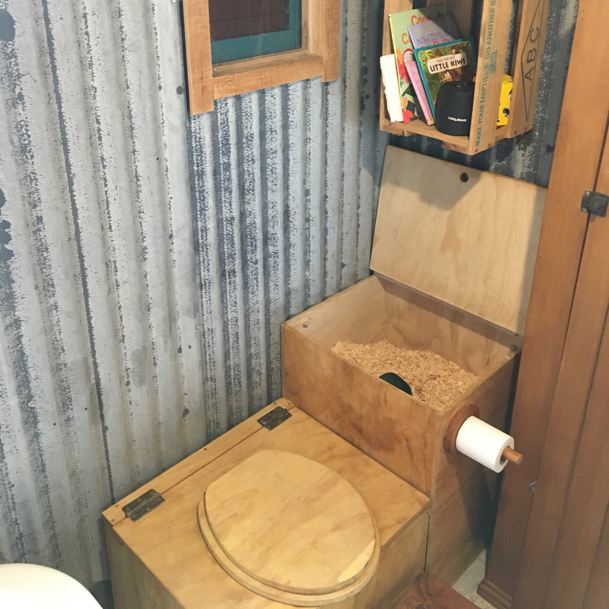 Wooden composting toilet set up with sawdust box with a small shelf above it.