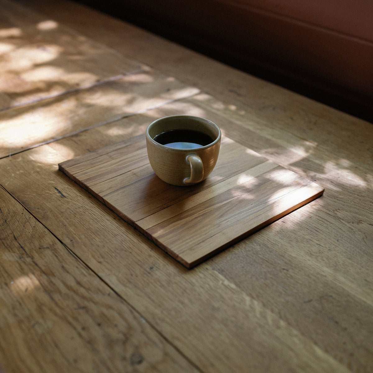 Ceramic cup of coffee on a wooden coaster with sunlight filtering through leaves